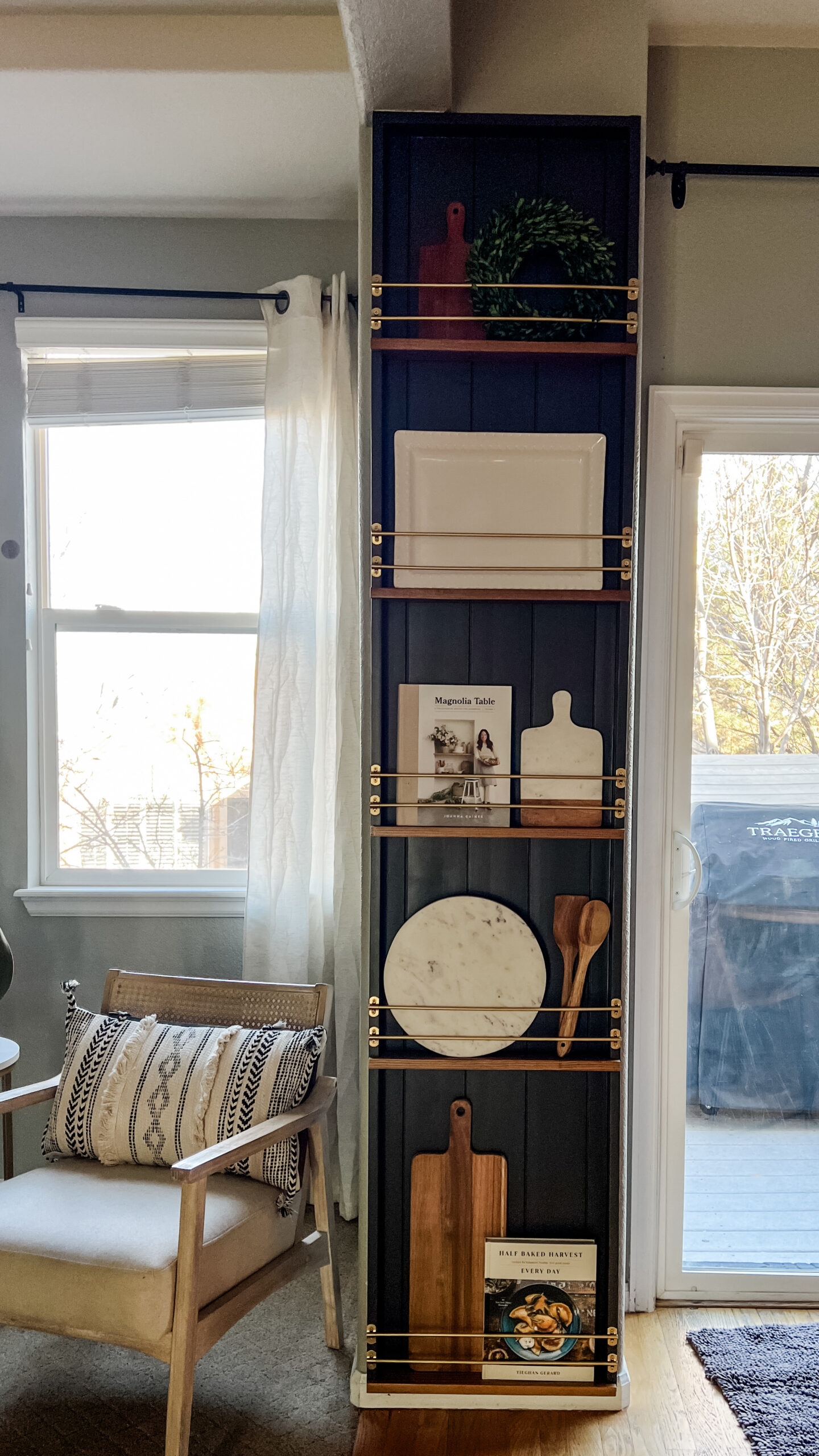 Dark painted shiplap with stained wood shelves and a metallic tipping rail on a narrow wall displaying plates, cutting boards and cookbooks.